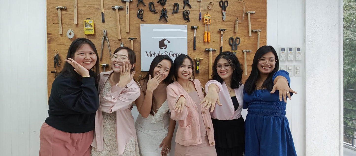 Bridal shower jewelry making group of women posing together in front of a wall with tools and a sign