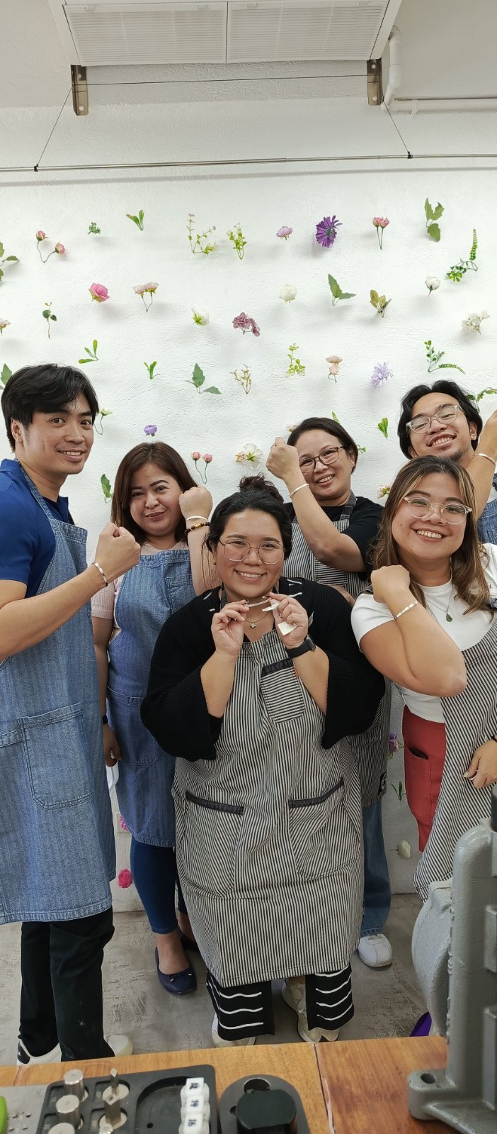 Employee engagement teambuilding jewelry making group of people posing together in front of a floral wall