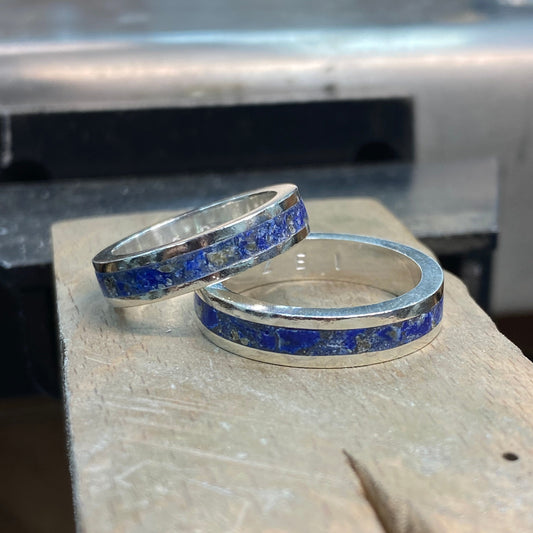 Two silver rings with blue inlay lapis lazuli on a stone surface