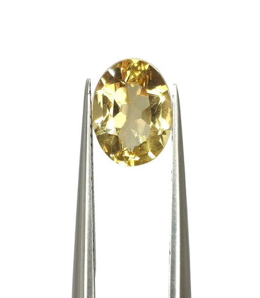 Yellow gemstone held by tweezers on a light gray background