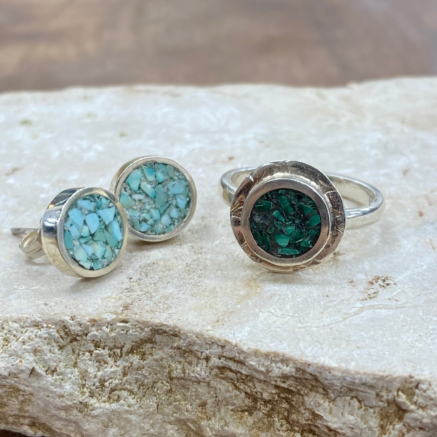 A sterling silver jewelry set featuring a ring and matching stud earrings, both with round turquoise-colored stone inlays. The ring has a textured silver bezel, while the studs have smooth bezels, displayed on a textured light stone slab.