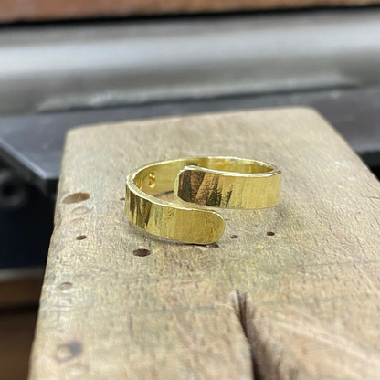 A polished gold-tone metal cuff ring with a hammered texture, resting on a rustic wooden block.
