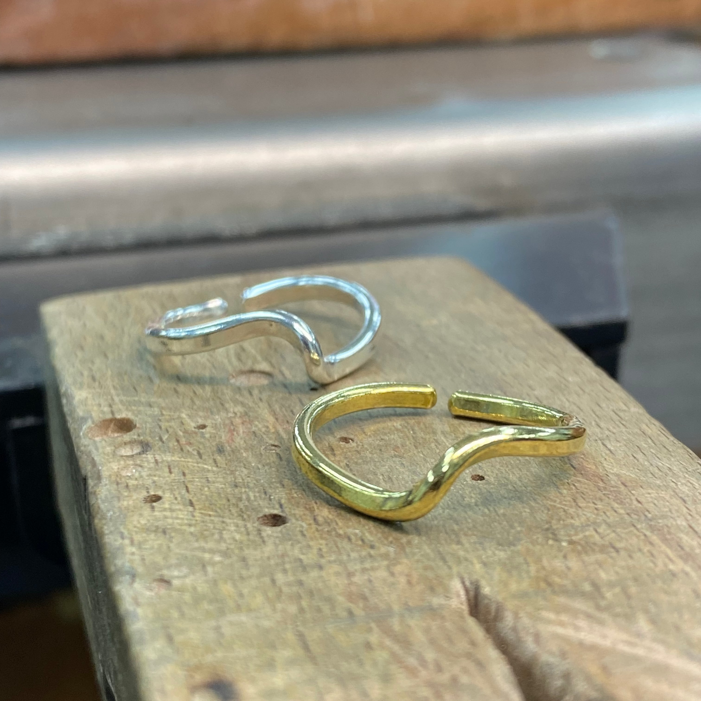 Two open hoop earrings, one in polished silver and one in polished yellow gold, displayed on a rustic wooden block.
