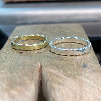 Two hammered metal rings, one gold and one silver, displayed side-by-side on a rustic wooden block.