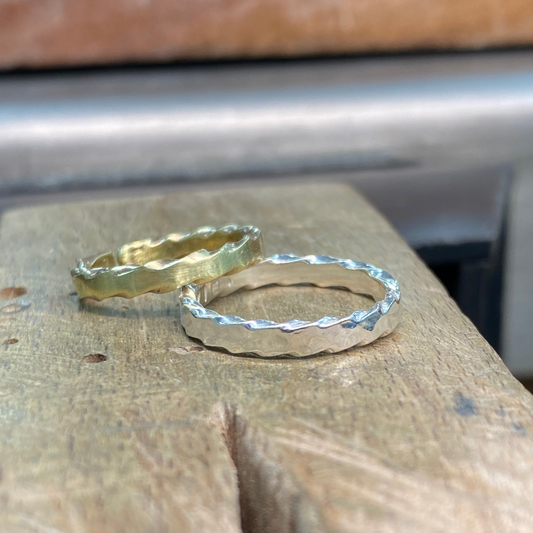 Two hammered metal rings, one gold and one silver, resting on a rustic wooden surface.