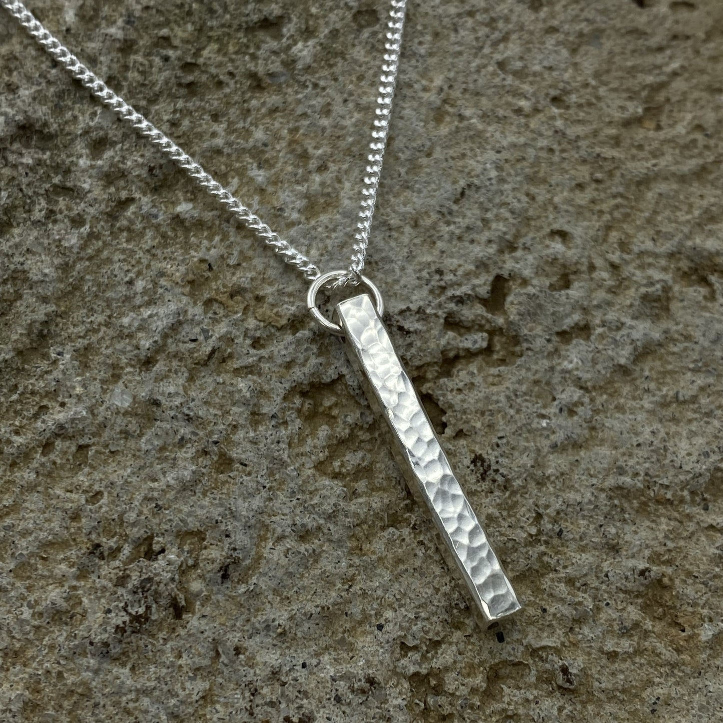 Silver necklace with a textured pendant on a stone surface
