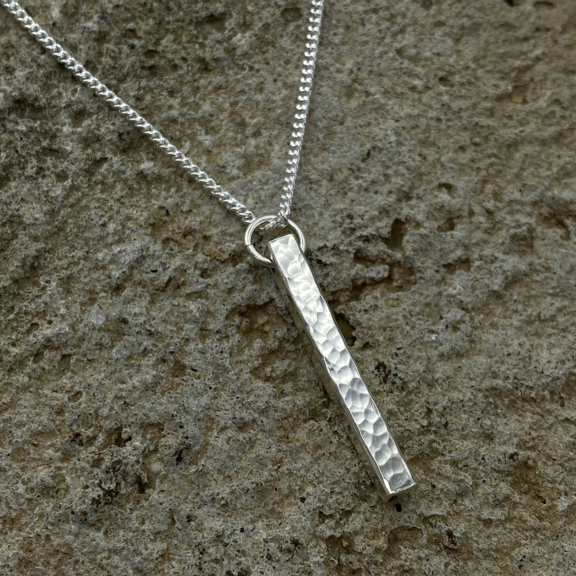 Silver necklace with a textured pendant on a stone surface