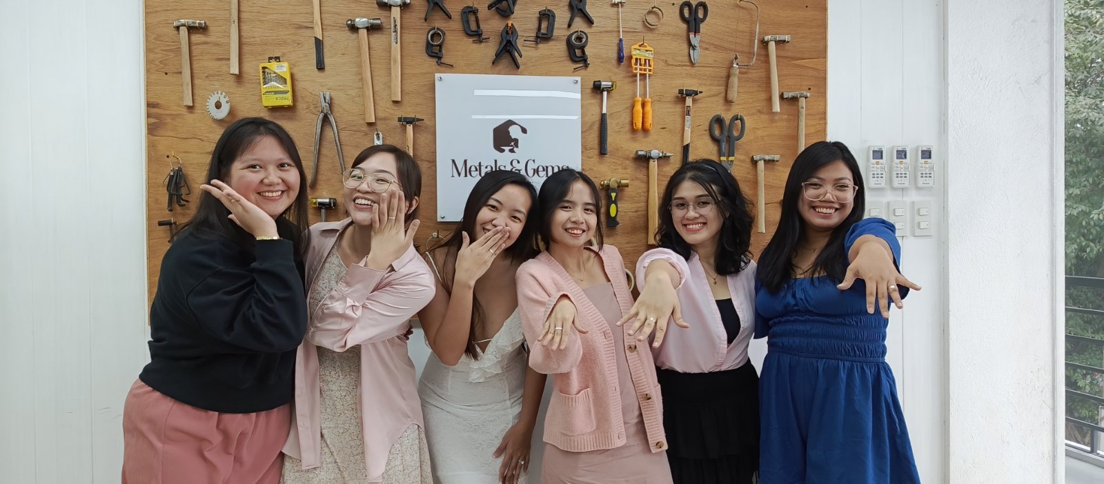 Bridal shower jewelry making group of women posing together in front of a wall with tools and a sign 