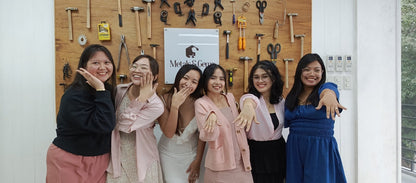 Bridal shower jewelry making group of women posing together in front of a wall with tools and a sign 